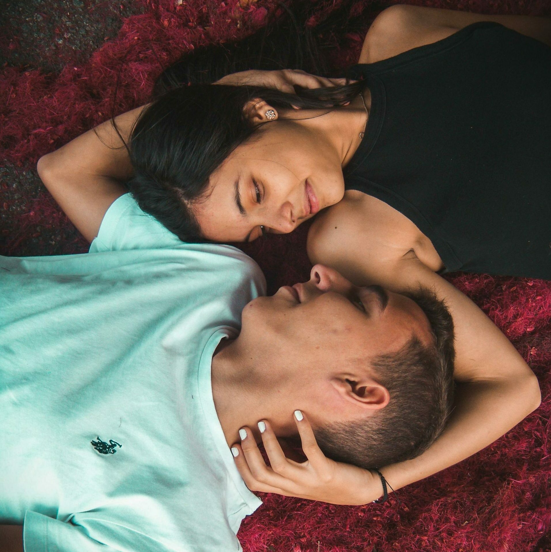 Young couple embracing on vibrant red grass, displaying intimacy and relaxation.