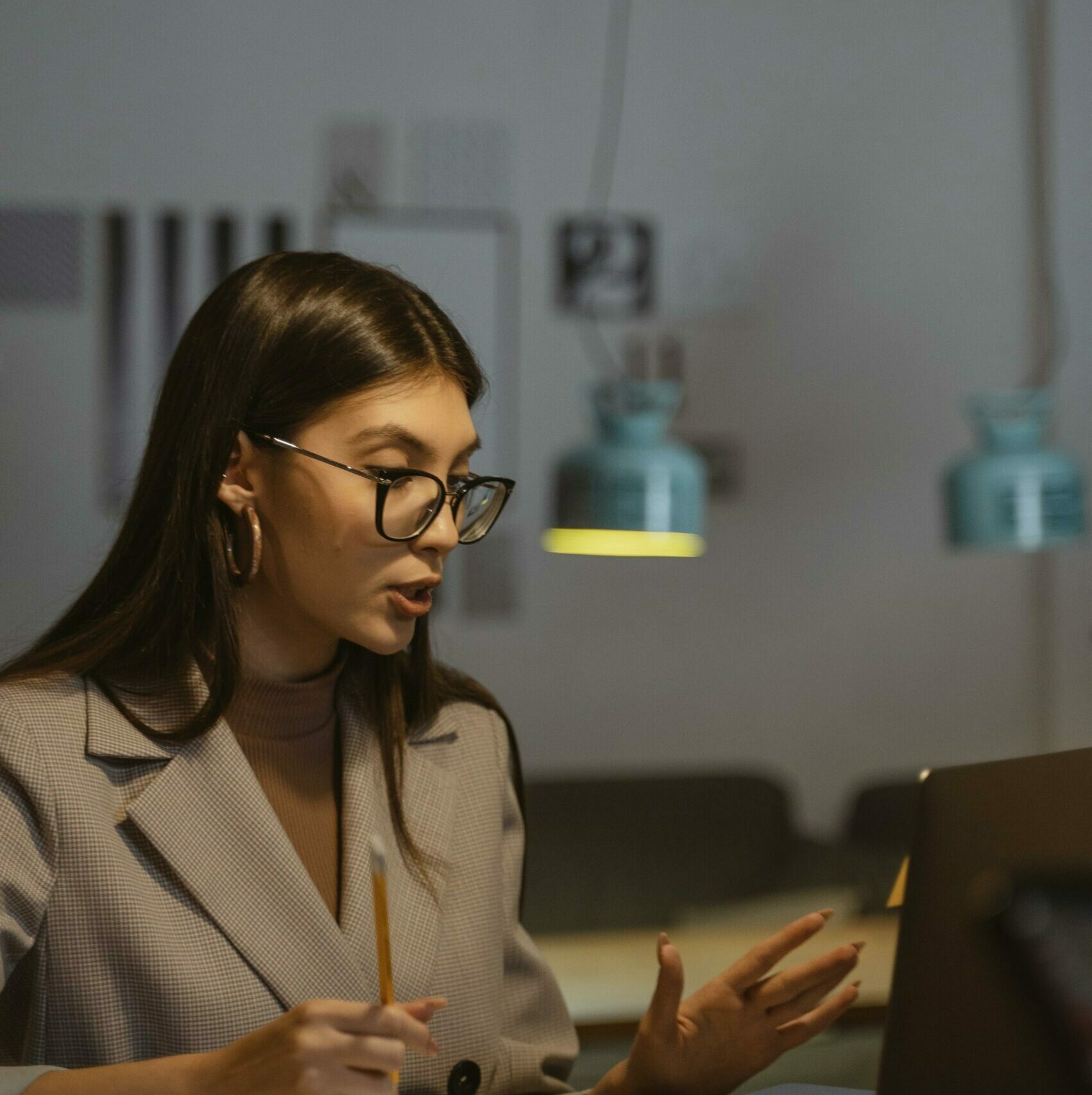 A young businesswoman working late at her desk, engaged in an online meeting with a laptop, notebook, and smartphone.